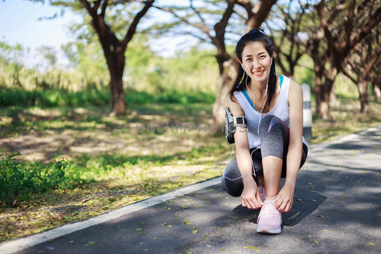 young sporty woman tying shoelaces while listening to music with earphones from her smartphone in the park 