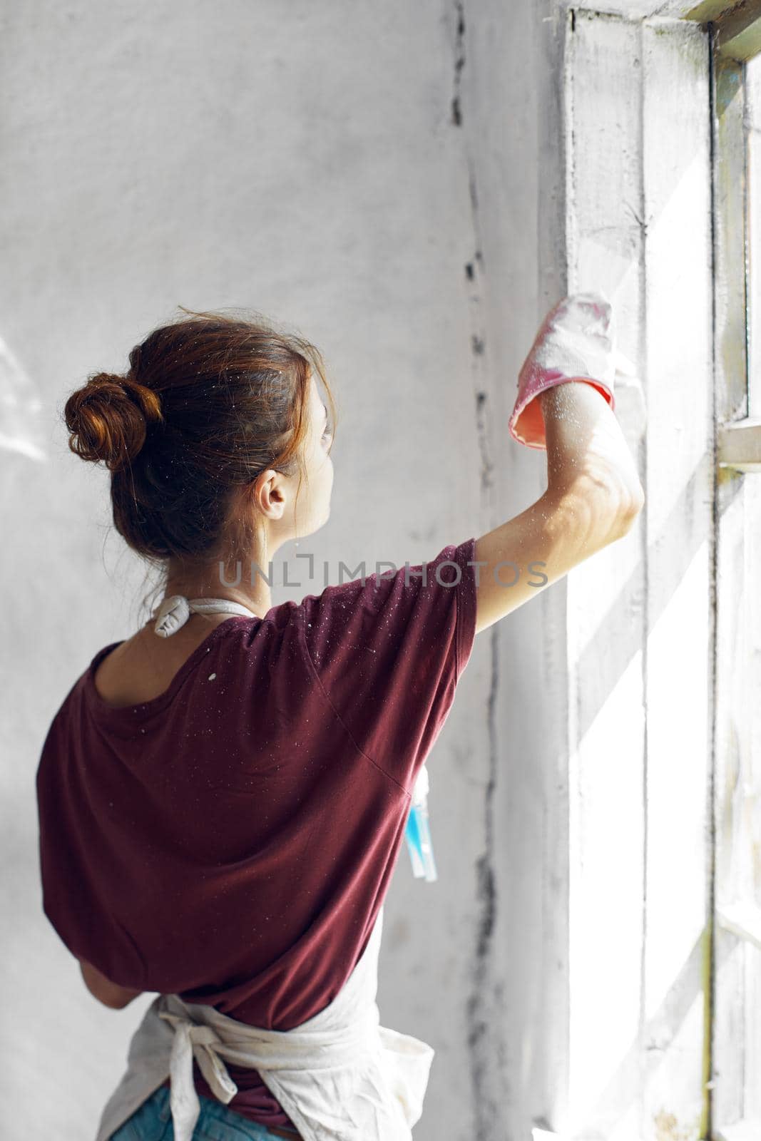 Woman in a white apron paints a window in a house interior renovation by Vichizh