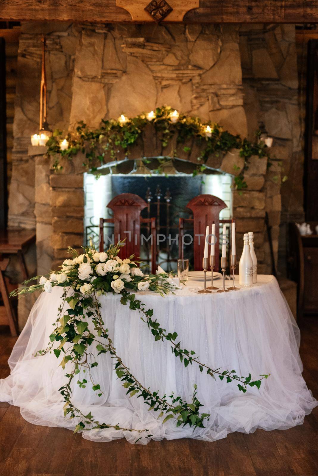 The presidium of the newlyweds in the banquet hall of the restaurant is decorated with candles and green plants, wisteria hangs from the ceiling