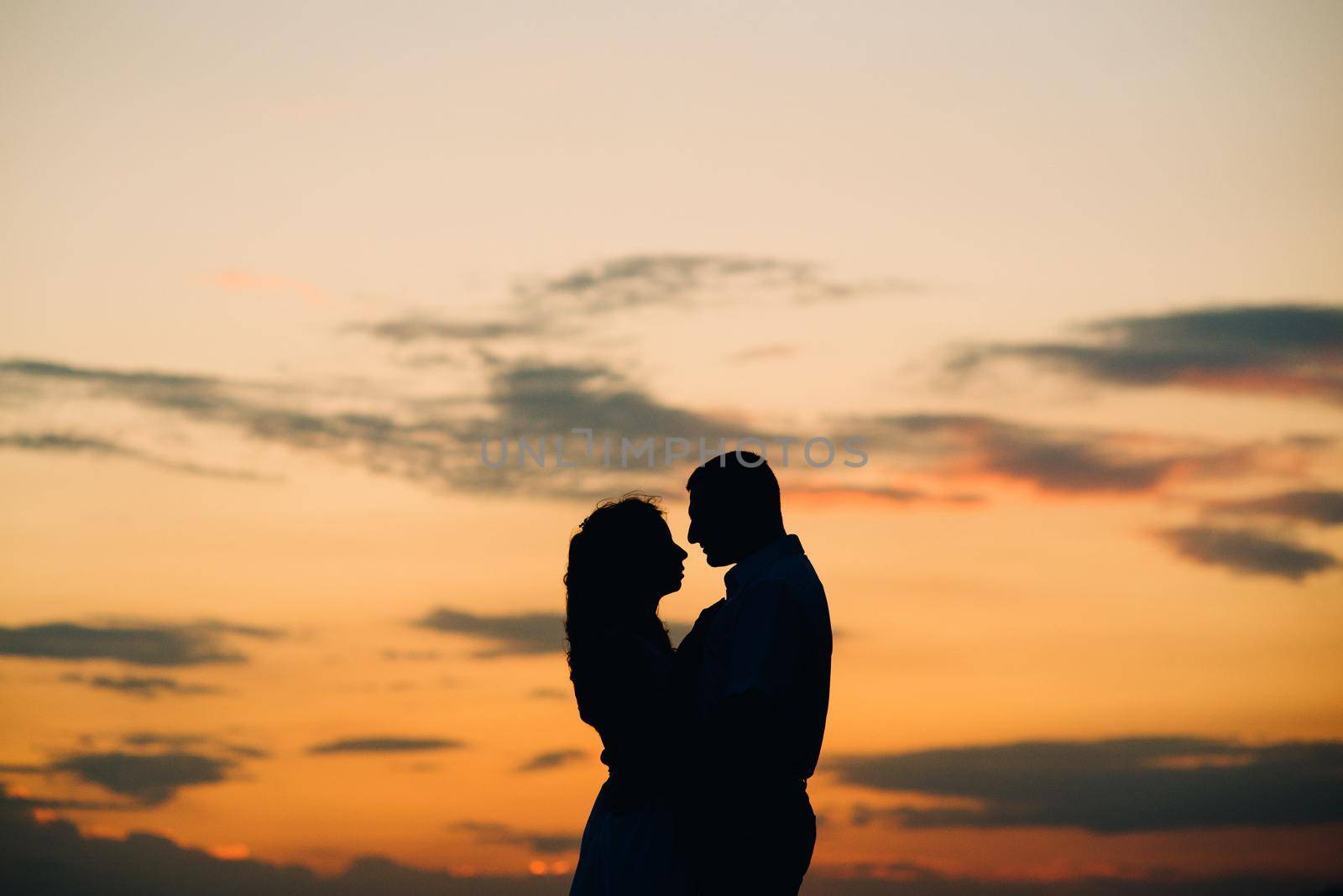 silhouettes of a happy young couple guy and girl on a background of orange sunset in the ocean