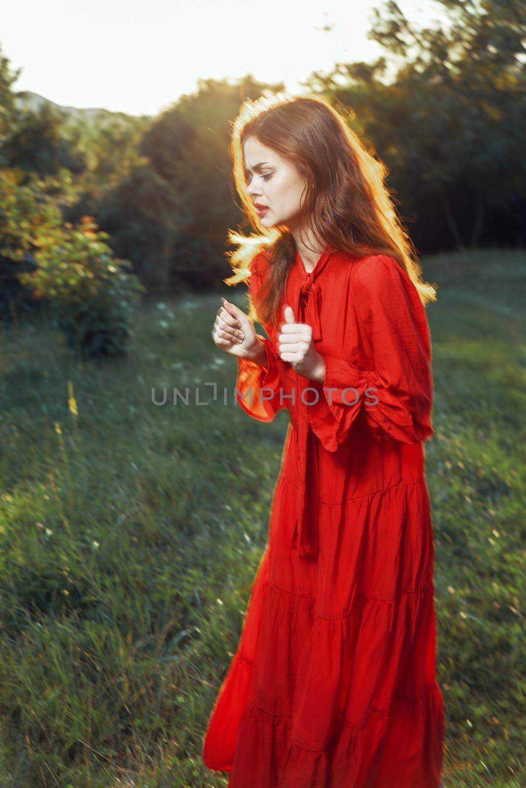 woman in red dress in field near tree posing summer. High quality photo