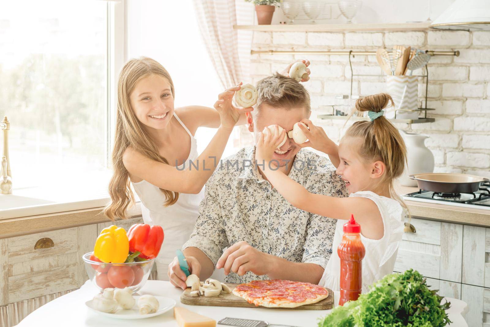 Dad with two small daughters preparing pizza with mushrooms in the kitchen