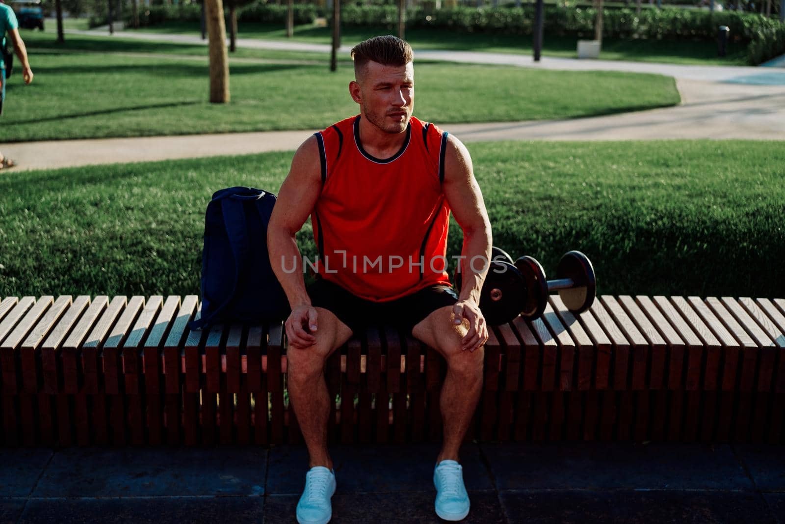 Cheerful male athlete in the park sits on a bench. High quality photo