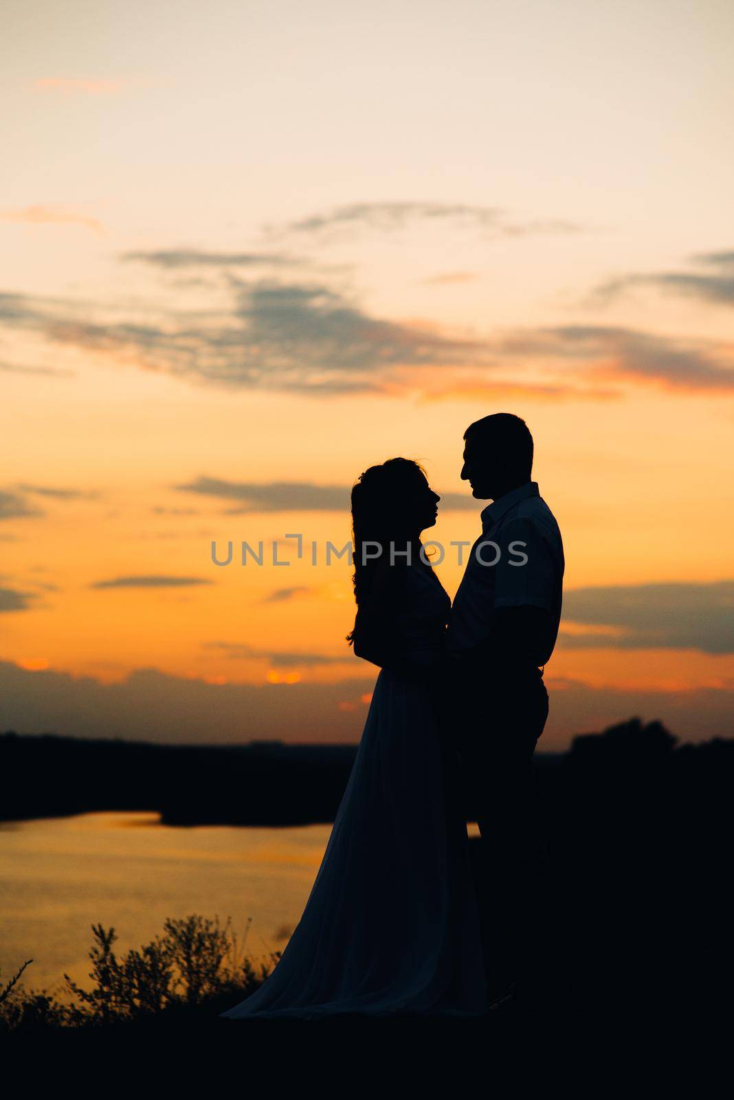 silhouettes of a happy young couple guy and girl on a background of orange sunset in the ocean