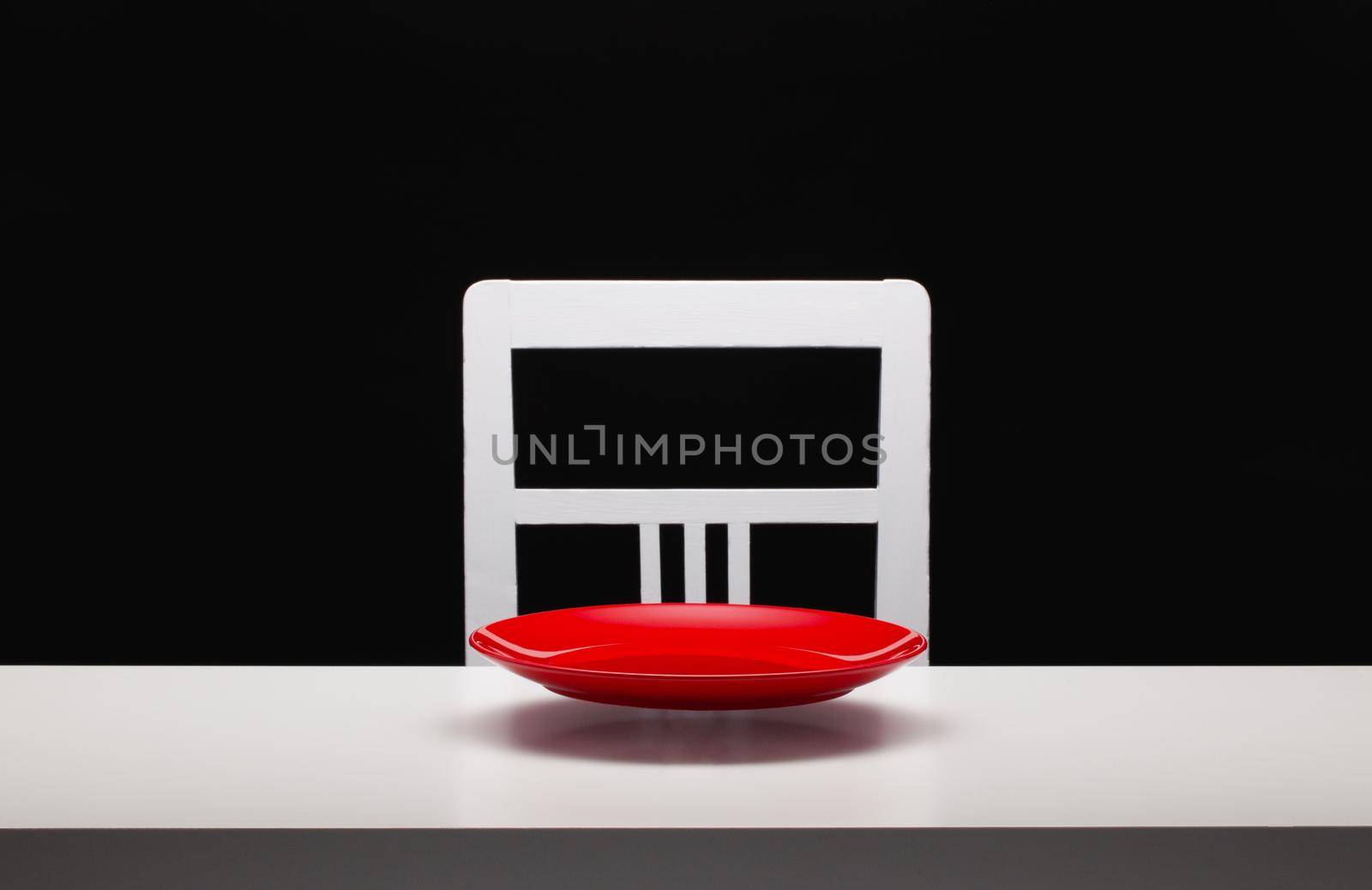 Levitating red plate over white table. White old chair and white table in the dark room.
