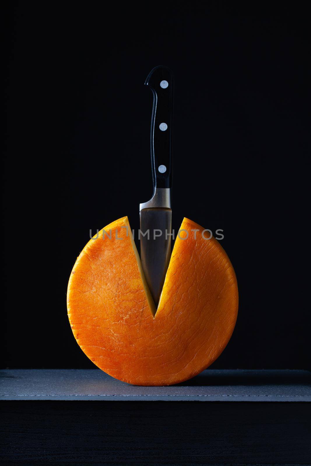 Big round of hard cheese with knife by CaptureLight