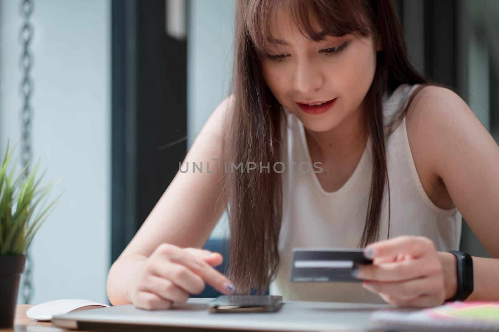 Portrait of young Asian woman smiling and holding a credit card and using a smartphone to shop online at home. online payment concept.