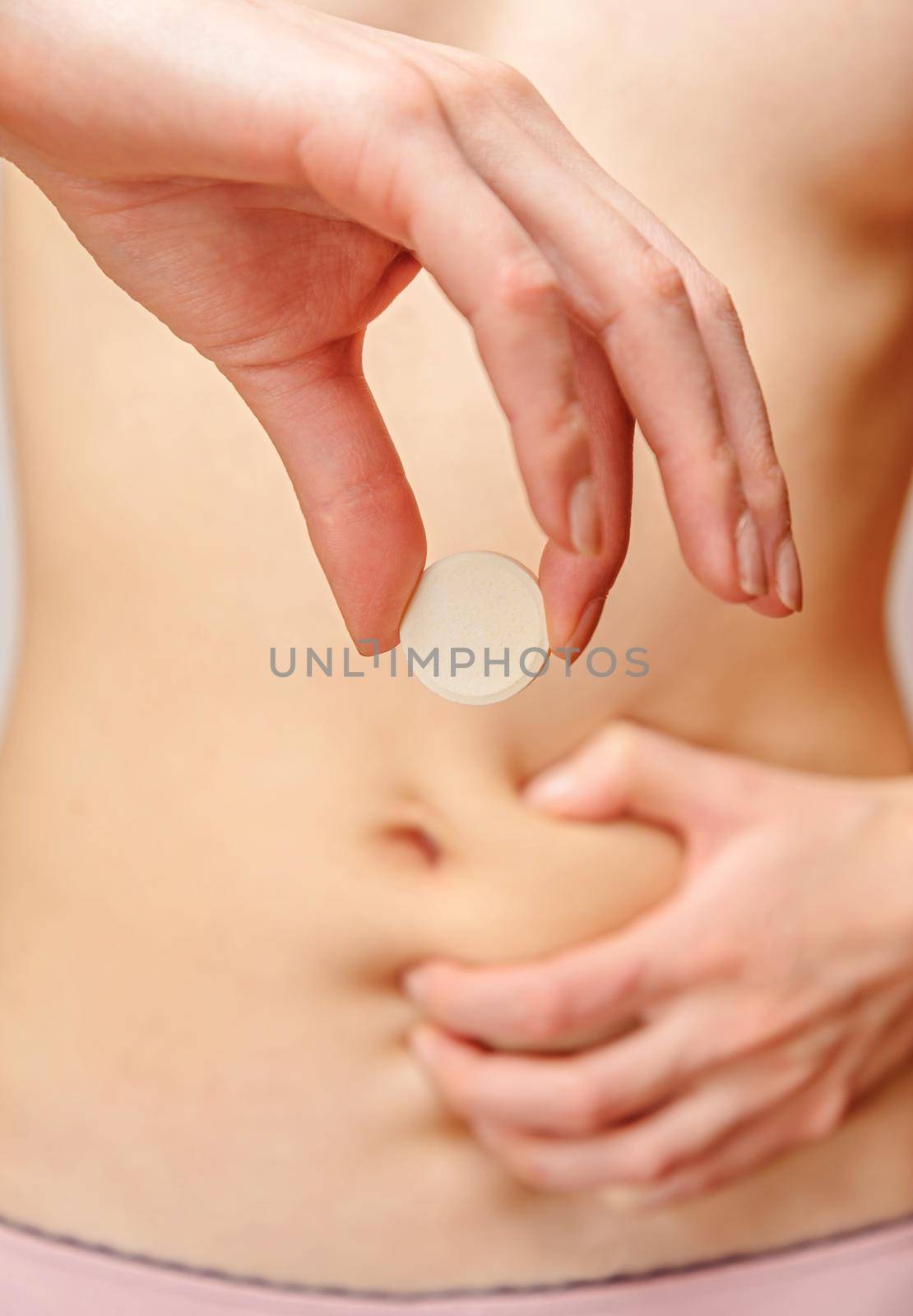 Woman holds a tablet from stomach pain in front of her abdomen