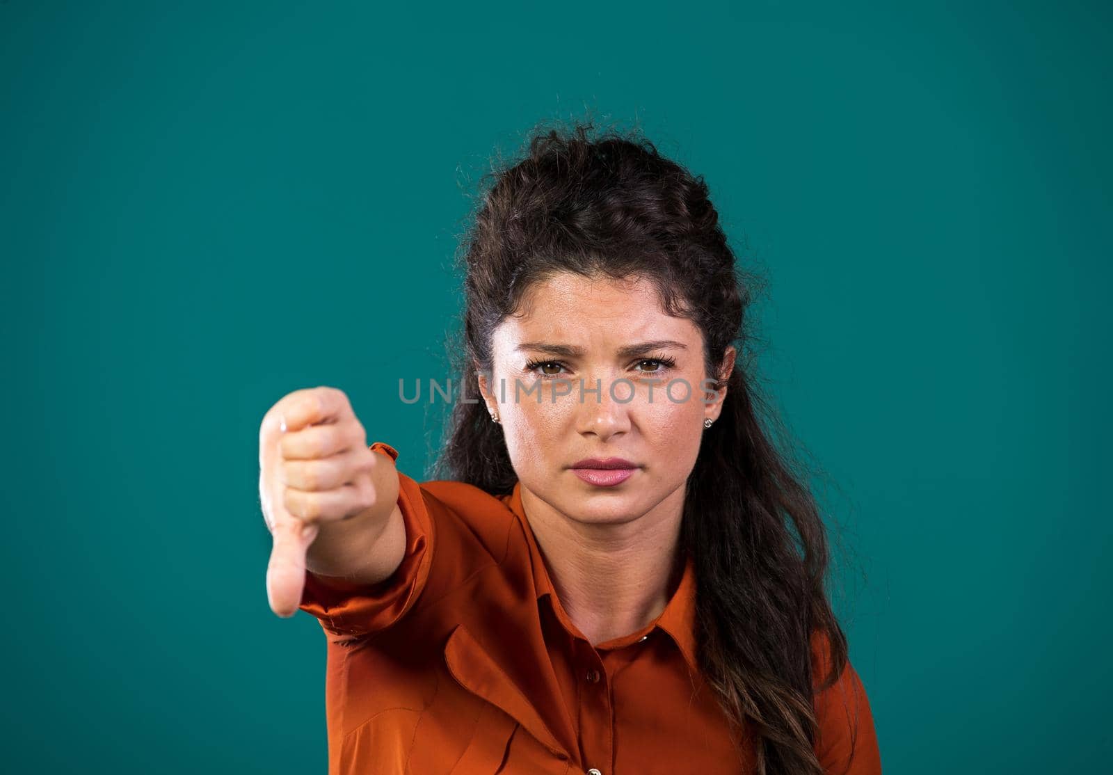 Pretty young woman showing thumb down as negative sign, hand gesture, in studio, against blue background