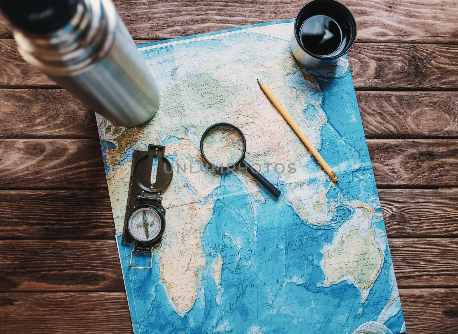 Map with a magnifying glass and compass on wooden background, top view. Concept of travel.