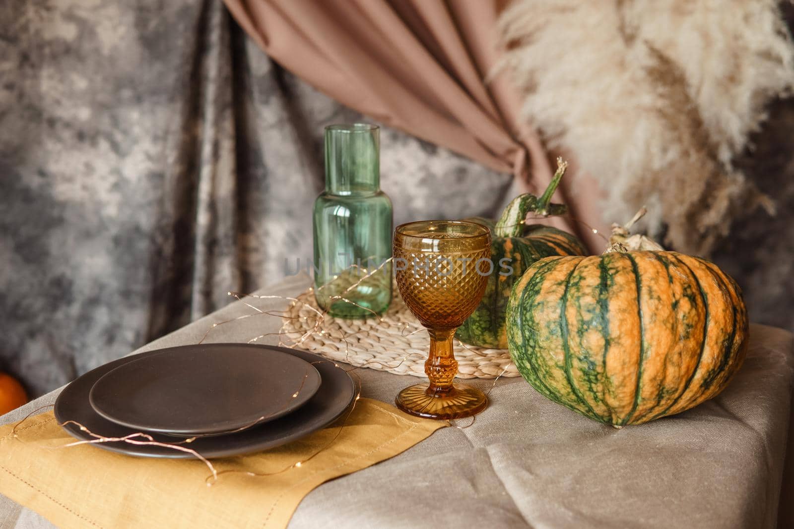 Autumn interior: a table covered with dishes, pumpkins, a relaxed composition of Japanese pampas grass. Interior in the photo Studio. Close - up of a decorated autumn table.