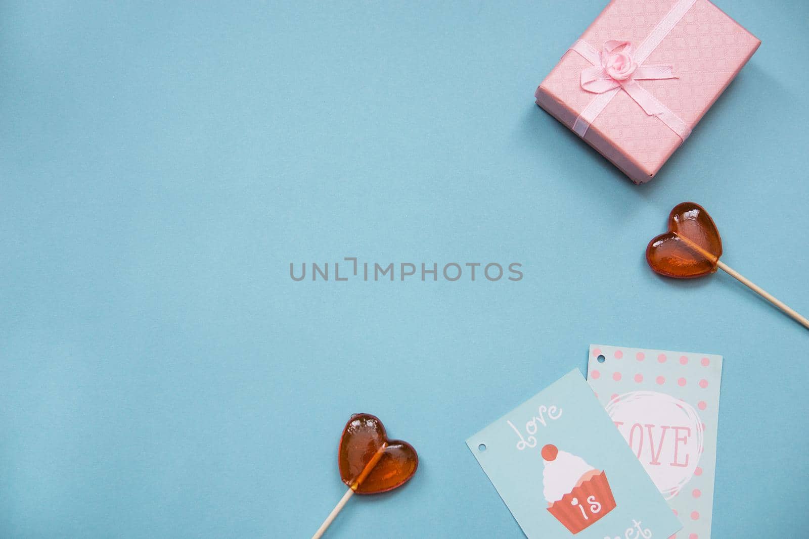 Lollipops in the form of hearts, a gift and greeting card on a blue background. Valentine's day, top view. Copy space. Mortgage the apartment. Text phrase Love and Love is sweet.