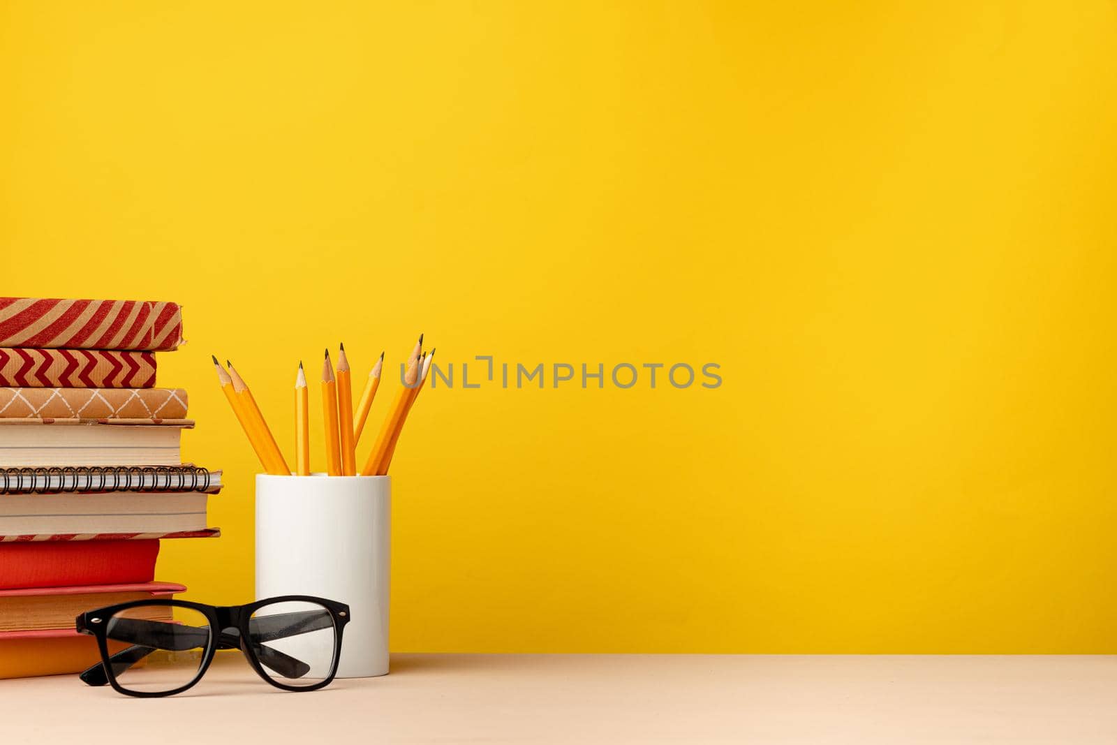 Cup of pencils and notepads on desk against yellow background, front view