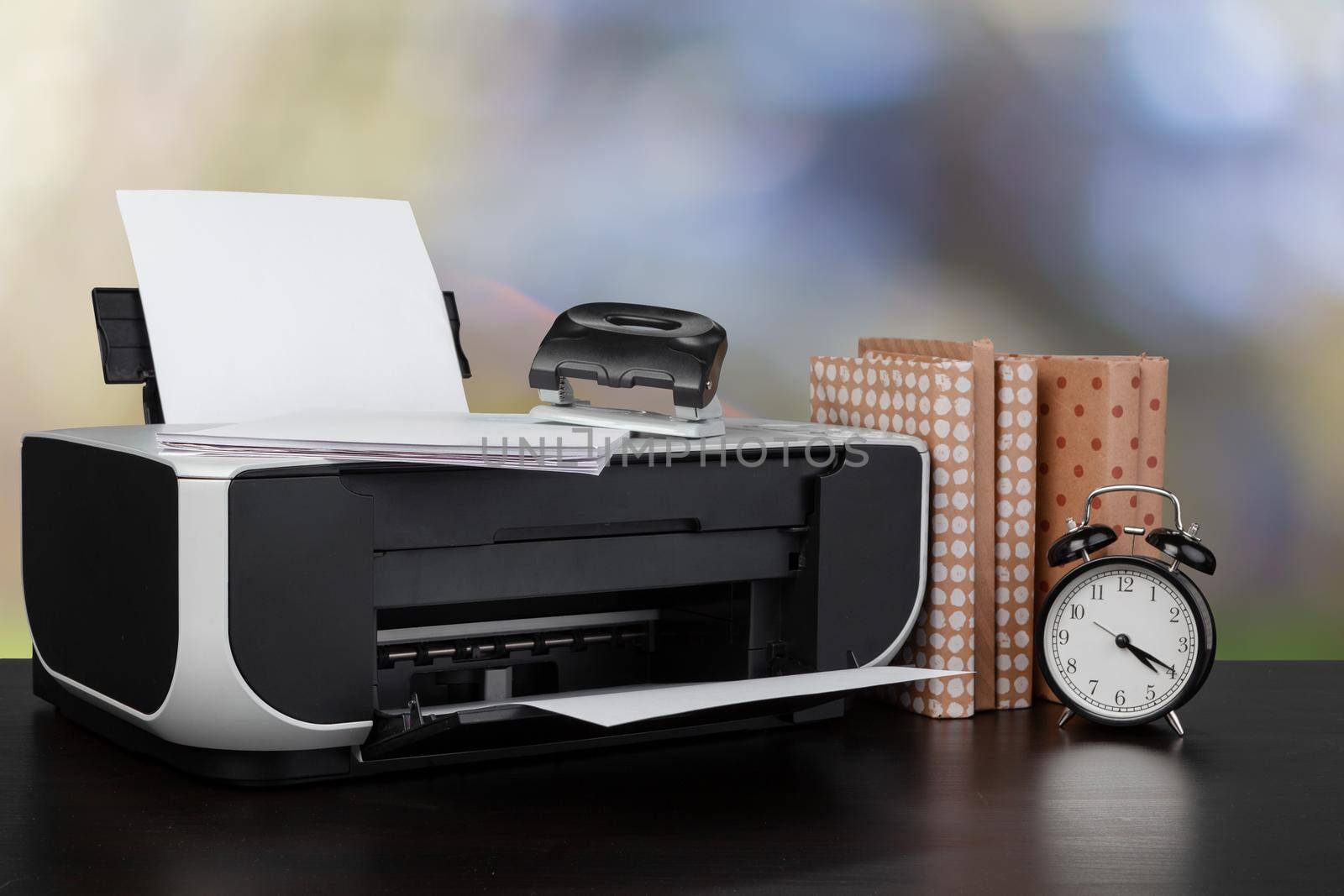Compact home printer on desk with books against blurred background, close up