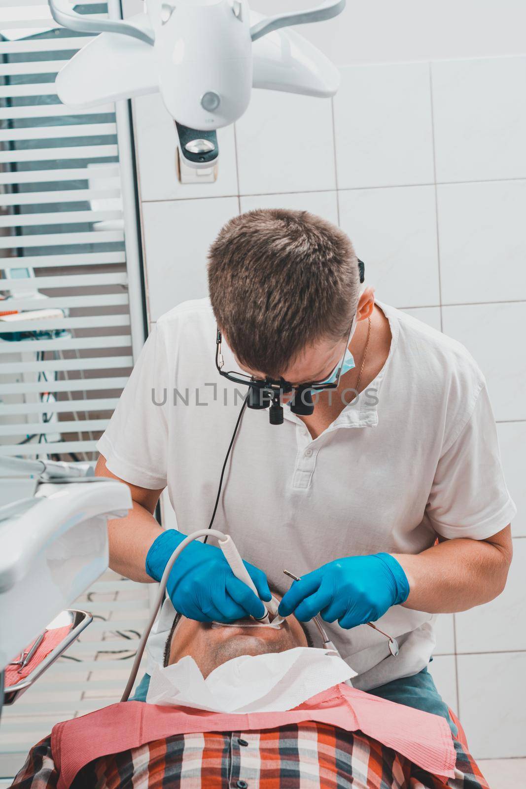 Dentist in the clinic,tartar removal procedure,the dentist in binoculars removes tartar in the patient's mouth.2020