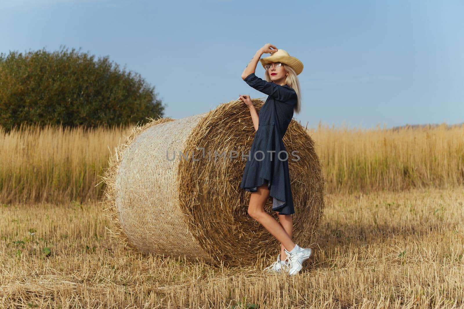 Beautiful girl villager posing in a dress near a bale of hay in a field