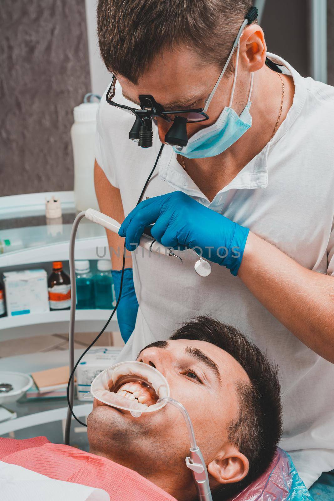 The procedure at the dentist,the dentist prepares the patient and tools to remove tartar, saliva ejector and retractor in the patient's mouth. by Niko_Cingaryuk