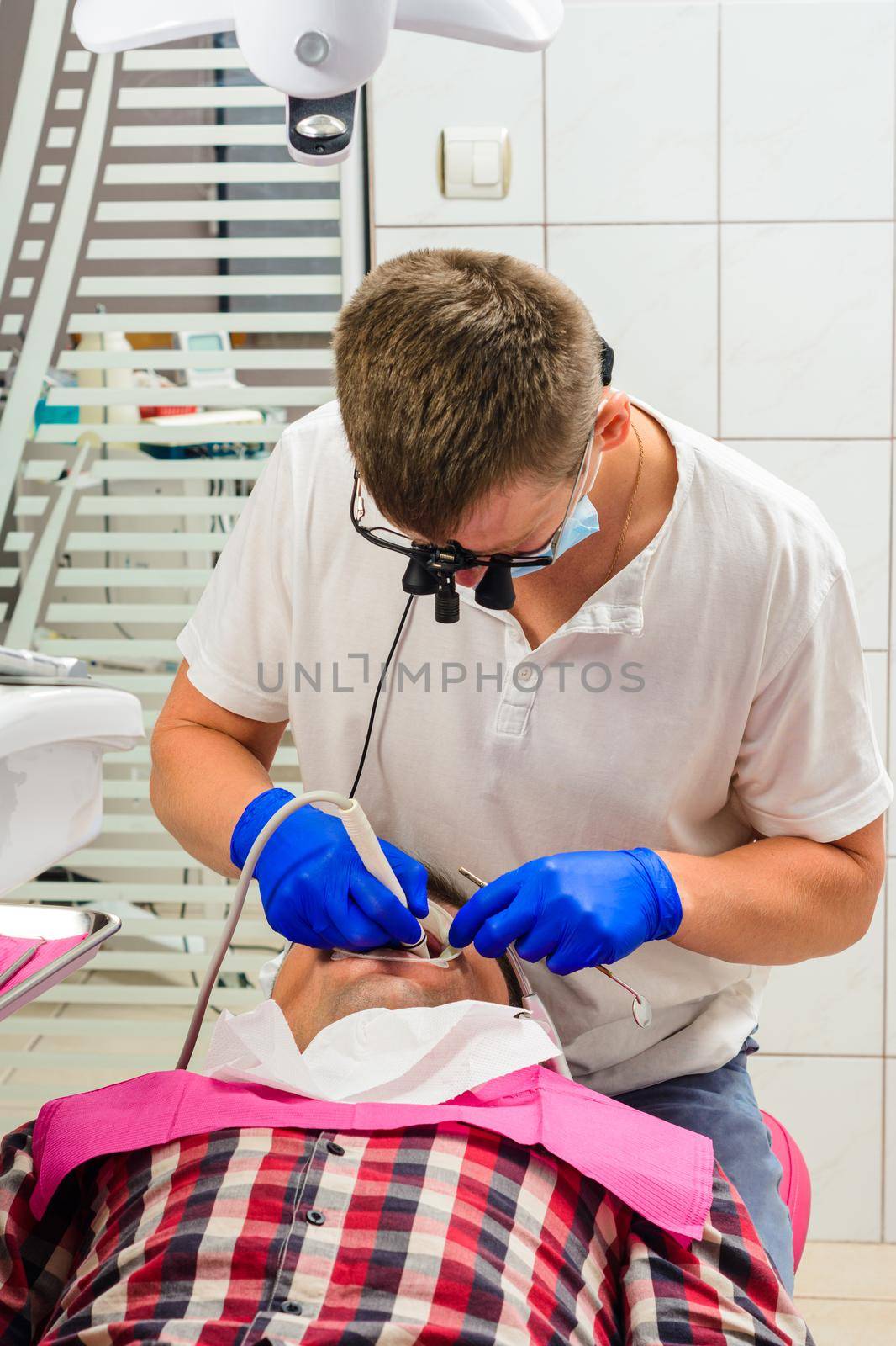 Dentist in the clinic,tartar removal procedure,the dentist in binoculars removes tartar in the patient's mouth. by Niko_Cingaryuk