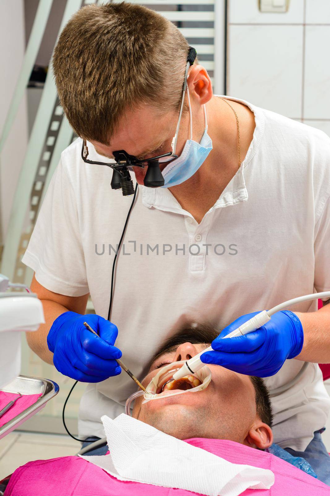 Dentist in the clinic,tartar removal procedure,the dentist in binoculars removes tartar in the patient's mouth.2020