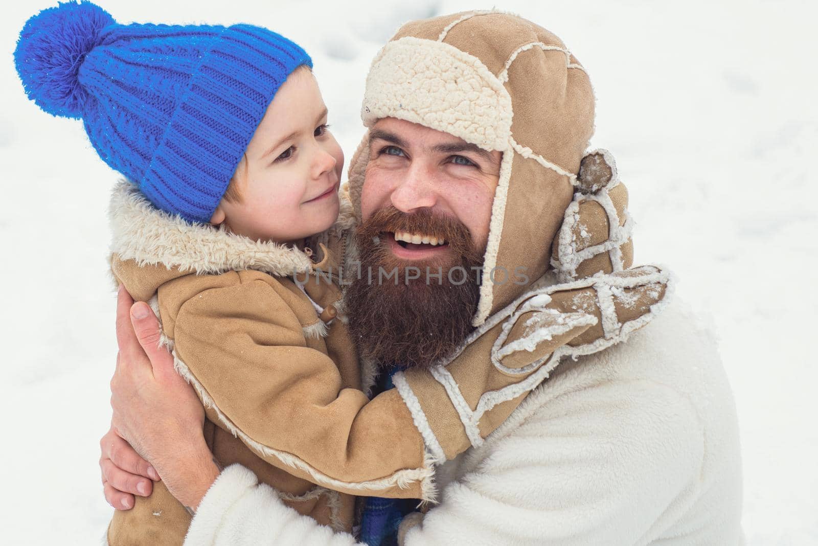 Winter, father and son play outdoor. Daddy and boy smiling and hugging. Happy son hugs his dad on winter holiday