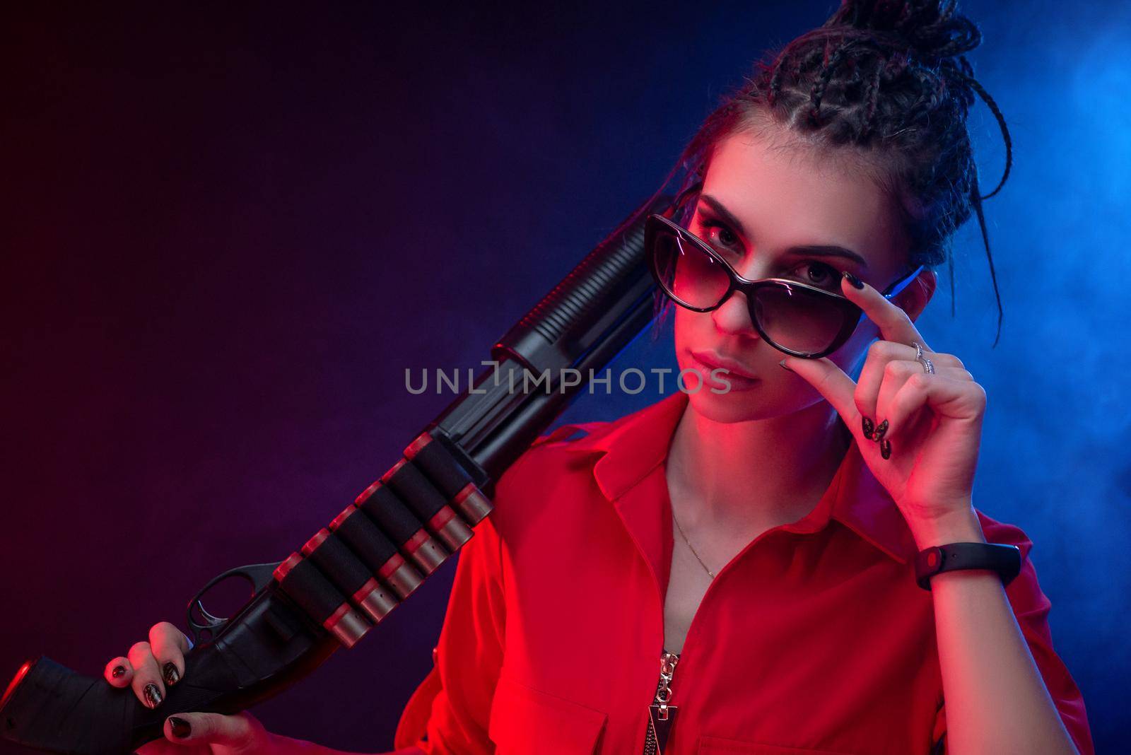 bright brunette in a red jumpsuit with a shotgun on a dark background in neon light