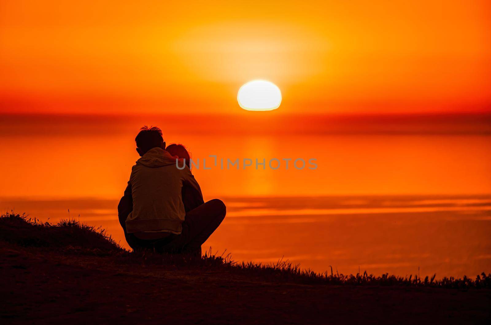 A red burning sunset over the sea with the silhouette of a young couple enjoying evening
