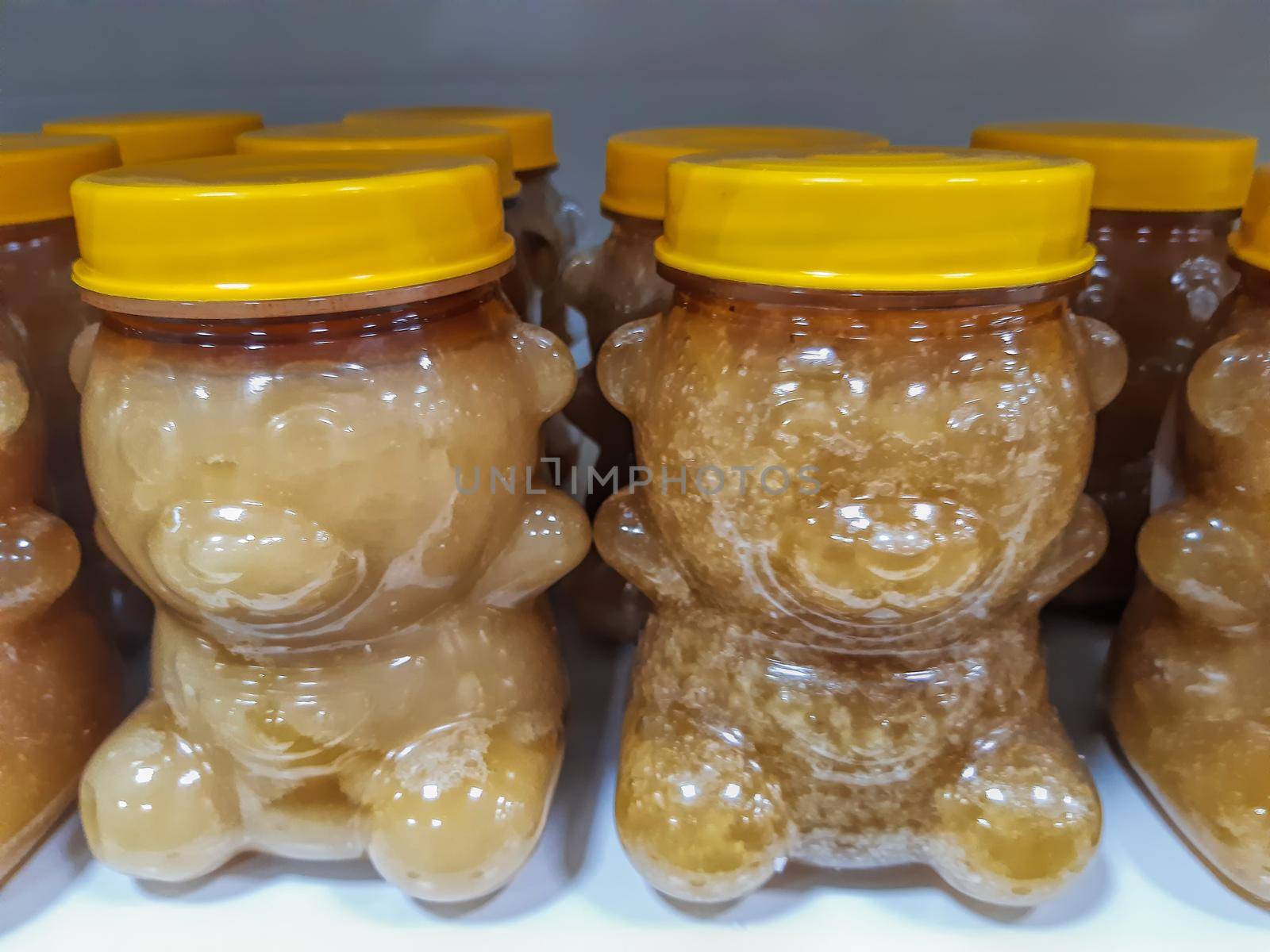 Many transparent plastic jars with yellow lids in the shape of a bear with different honey