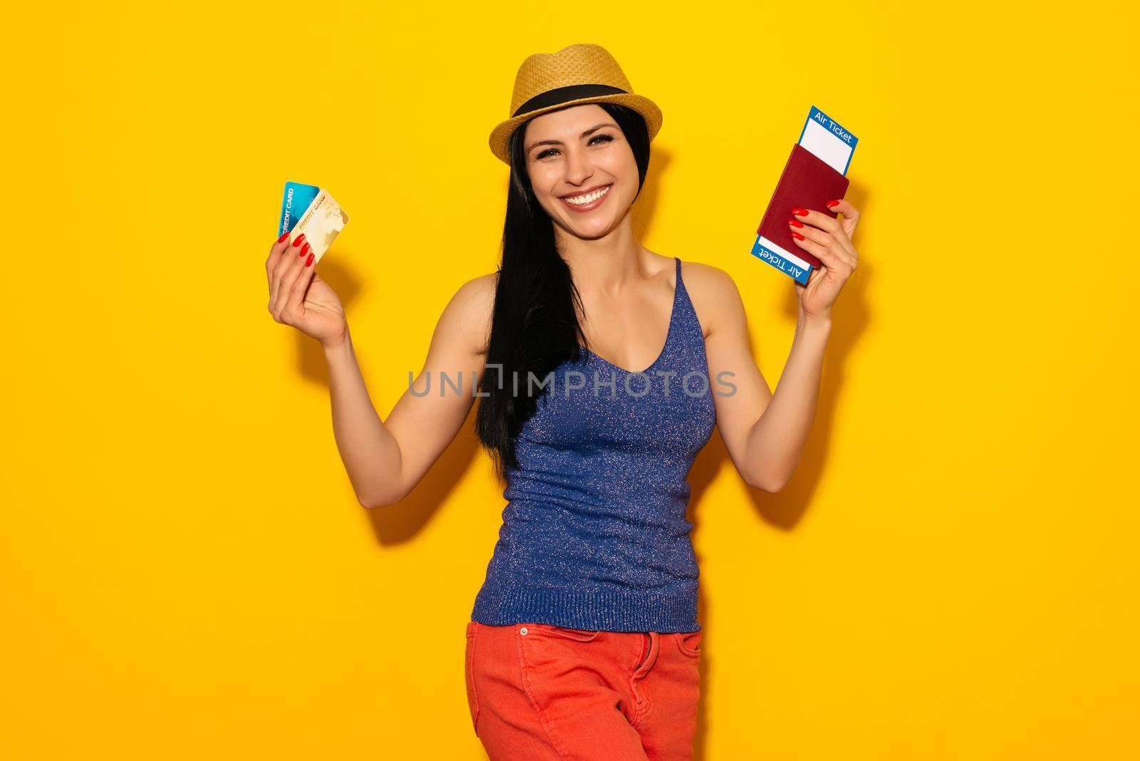 Young smiling excited woman student holding passport boarding pass ticket and credit card isolated on yellow background. Air travel flight - Image