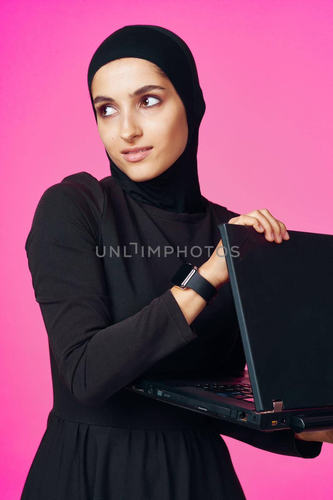 muslim woman in hijab with laptop technology learning pink background. High quality photo