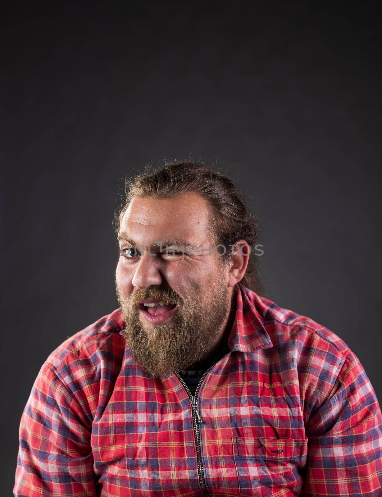 Funny guy with long hair and beard, wearing plaid shirt winking with eye in studio