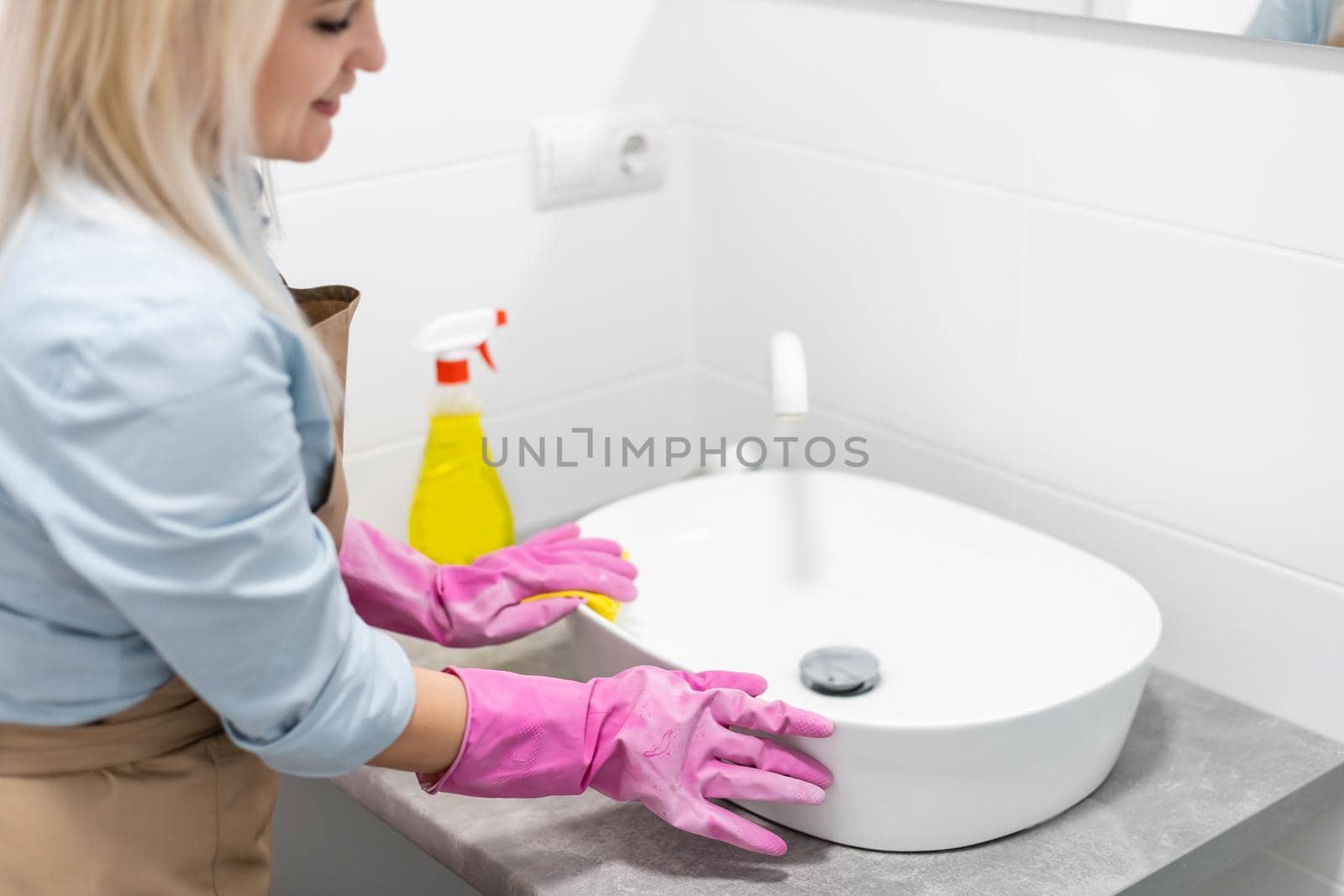 Housework and domestic lifestyle: woman doing chores in bathroom at home, cleaning wash basin and tap with spray detergent