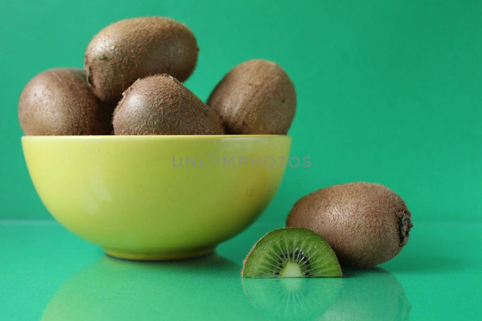 still life kiwi fruit in a yellow bowl plate and next to a kiwi copyspace slice.