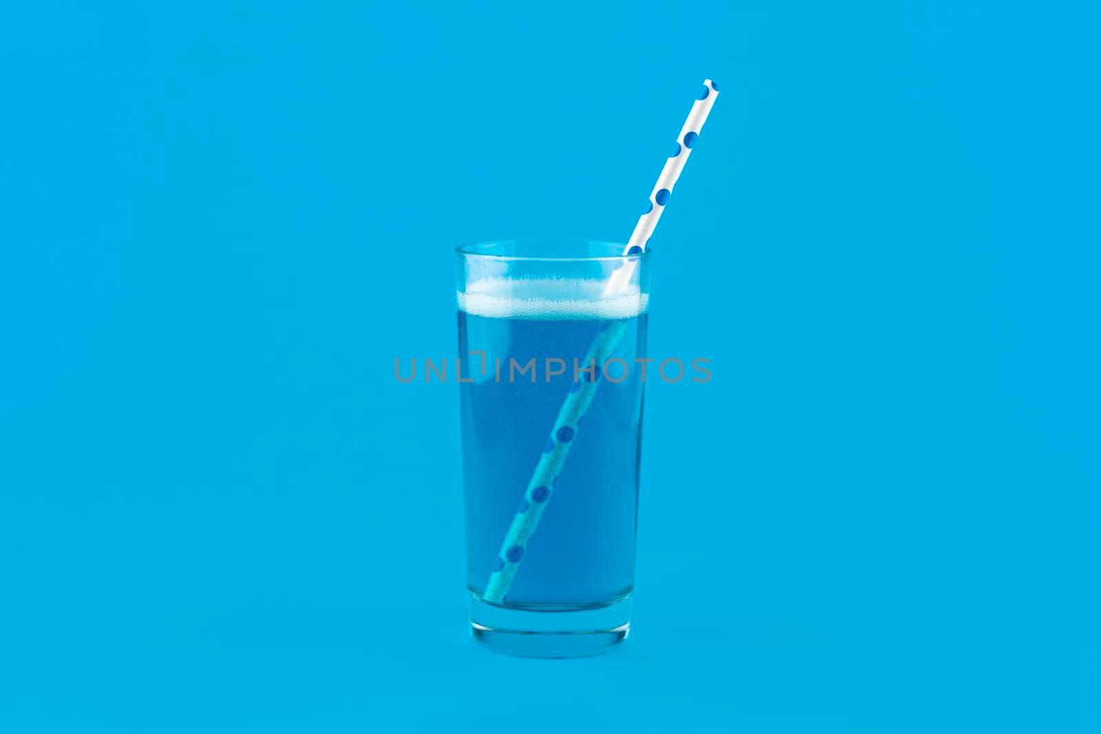 Blue lemonade with gas bubbles and a cocktail straw isolated on blue background. Blue Cocktail Drink monochrome banner with copy space.
