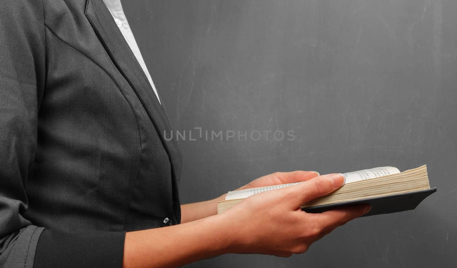 Teacher woman reading a book near a blackboard, side view