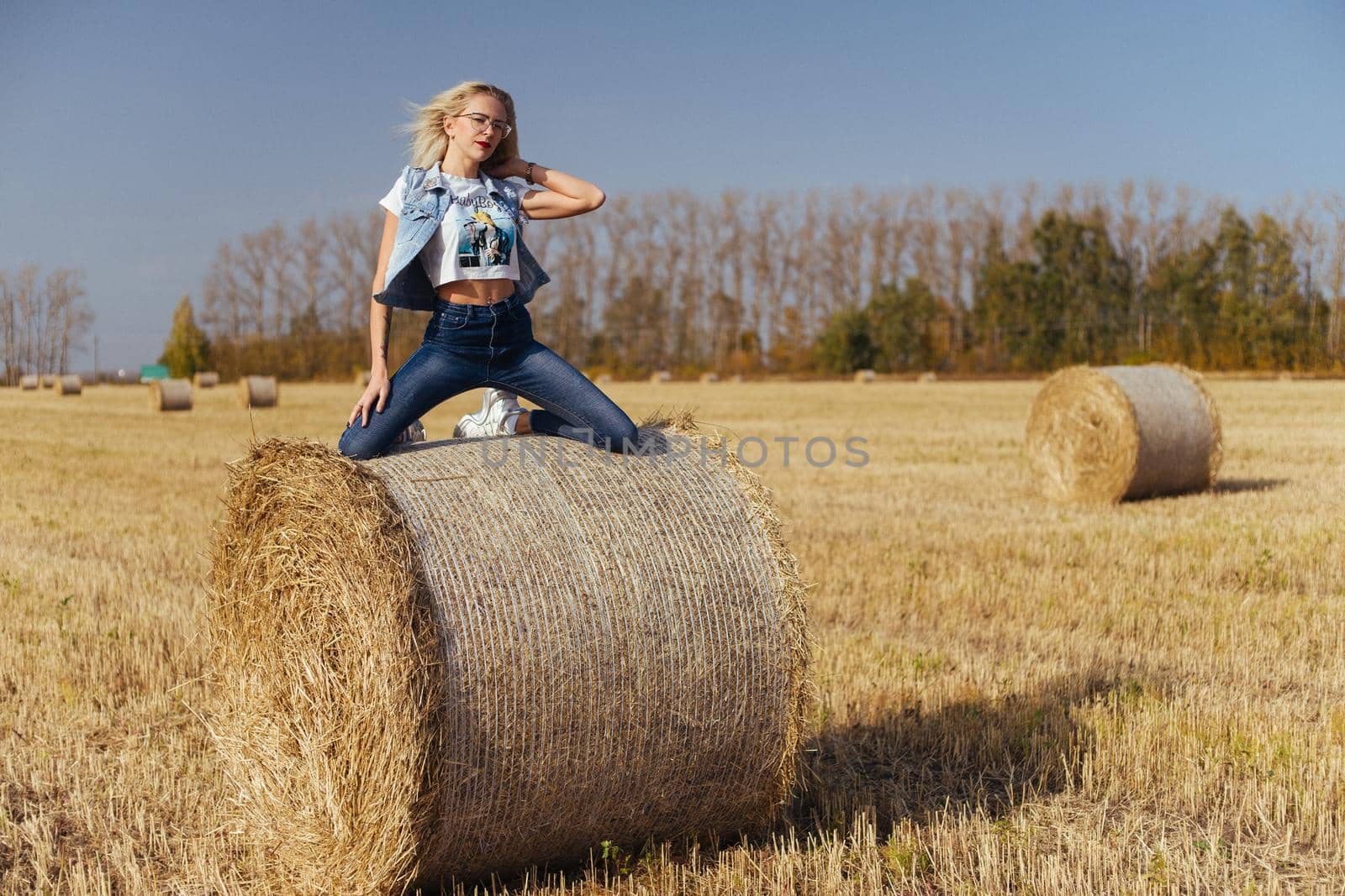 Beautiful girl villager posing in jeans on a bale of hay in a field