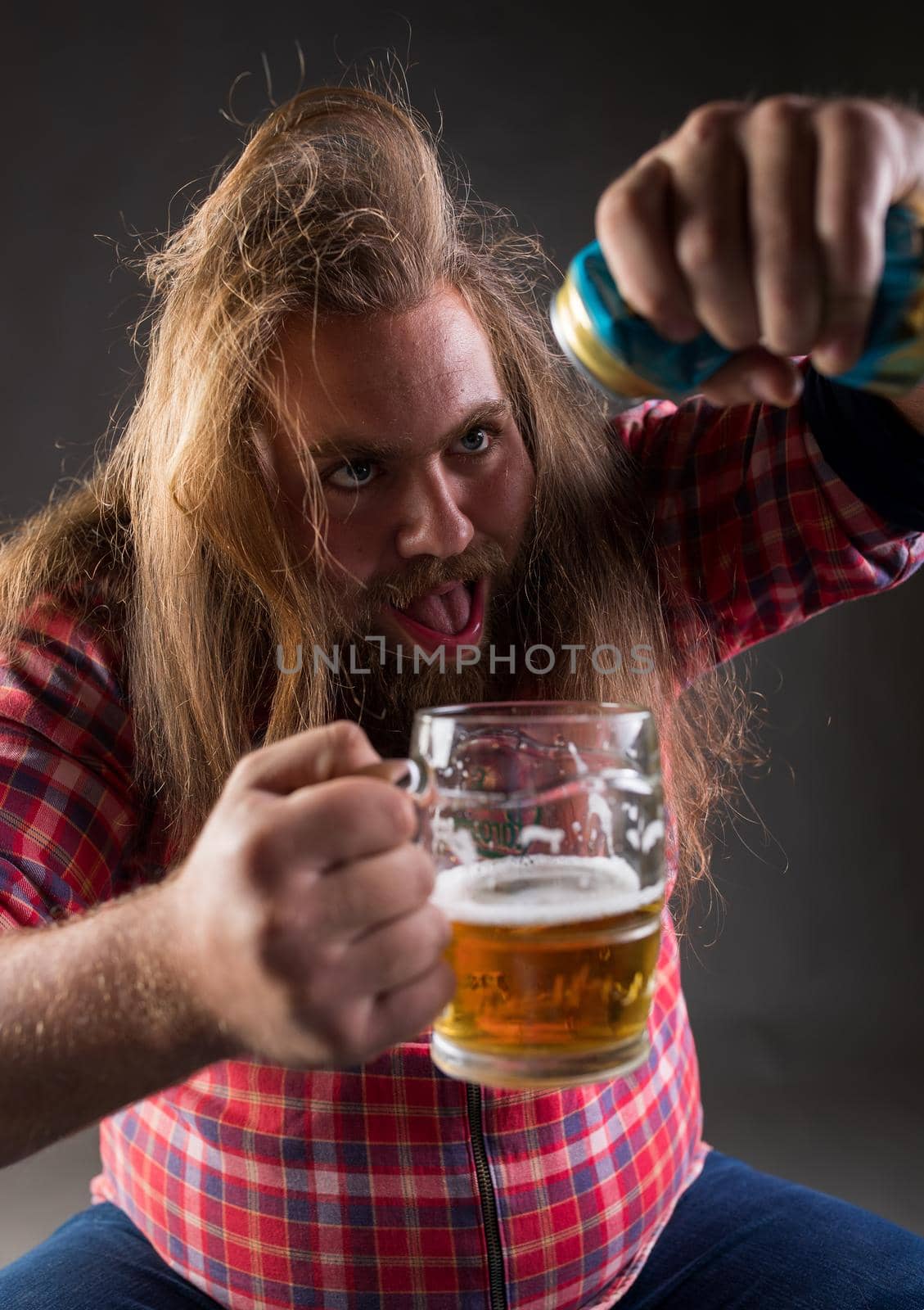 Messy drunk man pouring beer from can into mug in studio