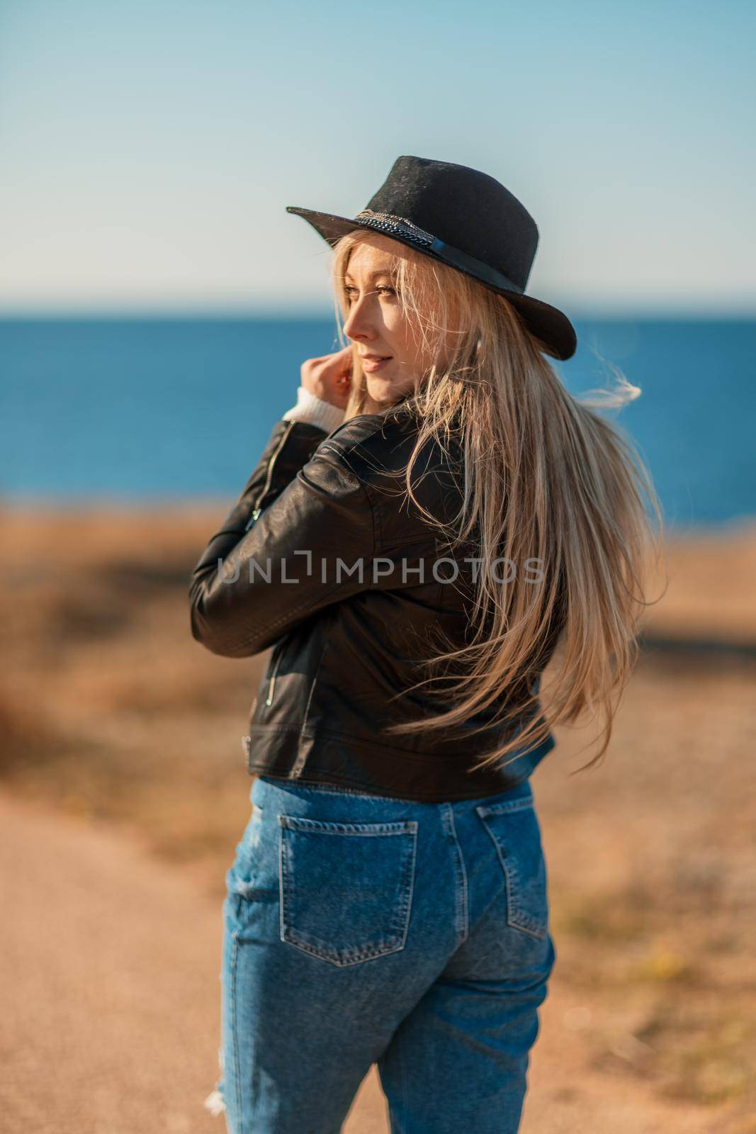 A blonde in a stylish black leather jacket walks along the seashore. by Matiunina