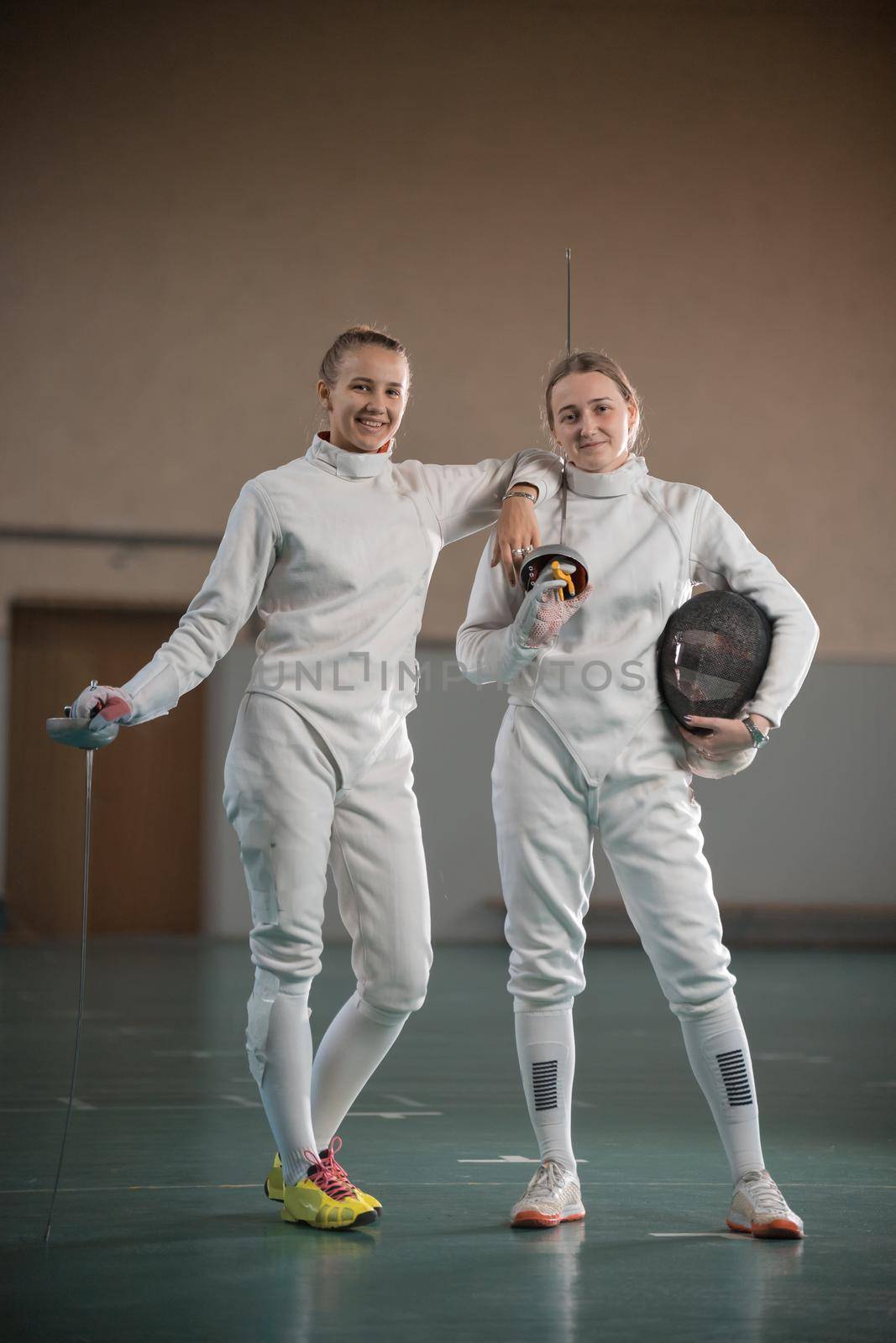 Two young women fencers looking at the camera and holding swords. Mid shot
