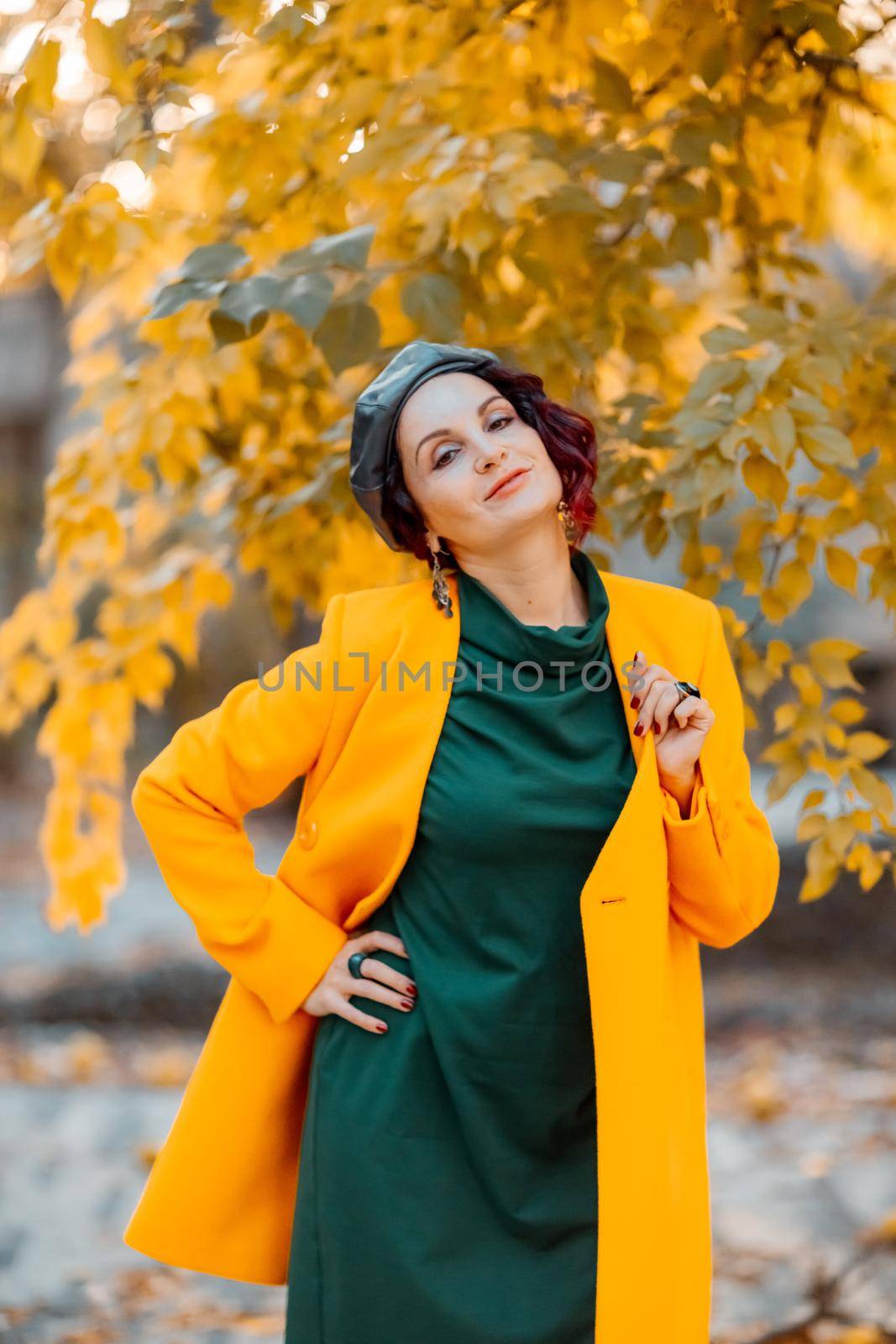 Beautiful woman walks outdoors in autumn. She is wearing a yellow coat and a green dress. Young woman enjoying the autumn weather. Autumn content. by Matiunina