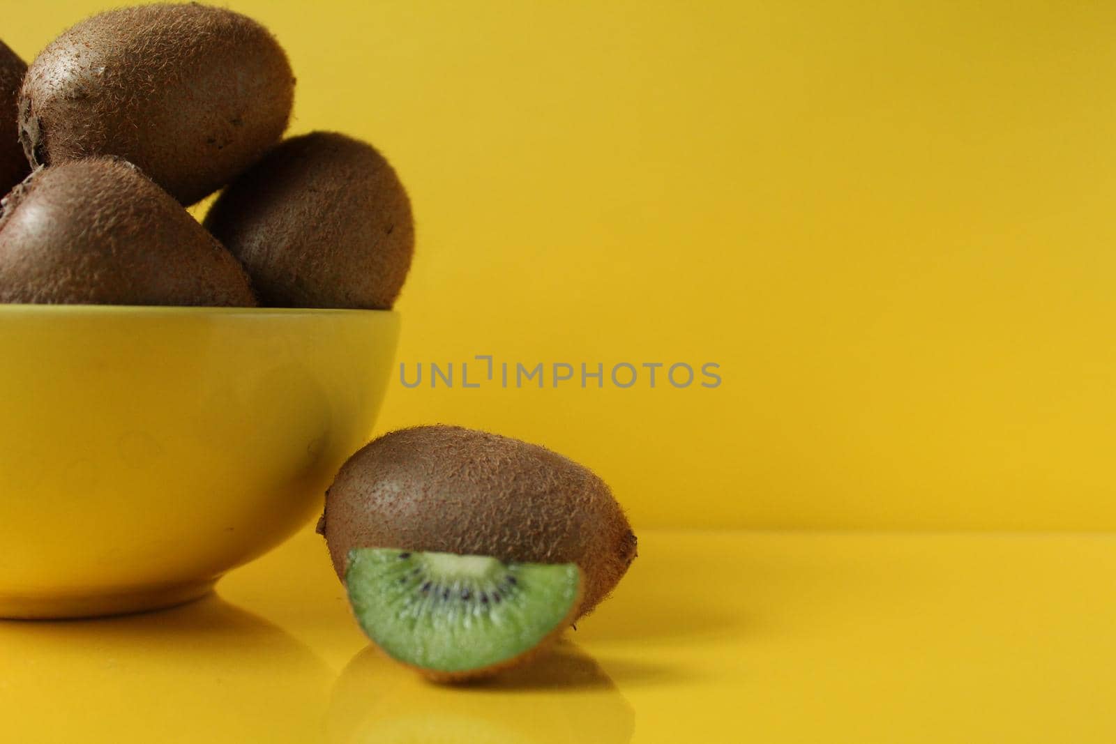 Still life of fruit trending illuminatiited yellow kiwi in a bowl plate of yellow and next pieces of kiwi yellow background copyspace.