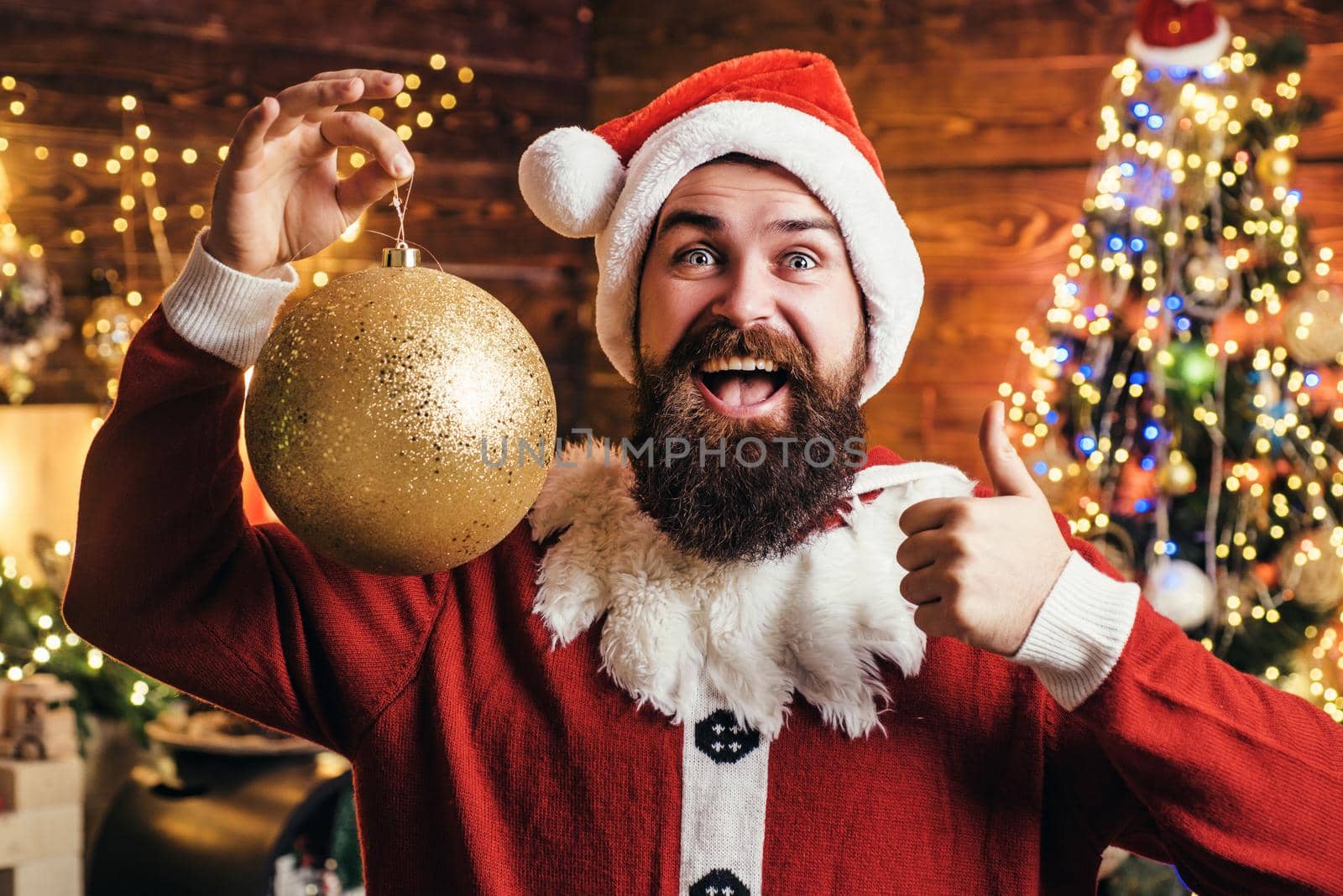 Crazy, funny Hipster Santa. Portrait of happy Santa with decorative toy balls near Christmas tree. Santa Claus man on Christmas
