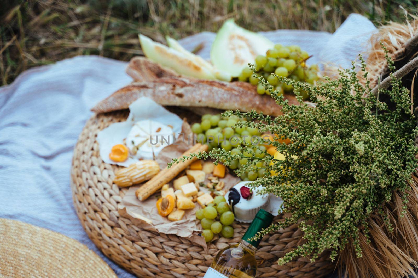 Wine and assorted products for the summer picnic are served on a blanket outdoors by Matiunina