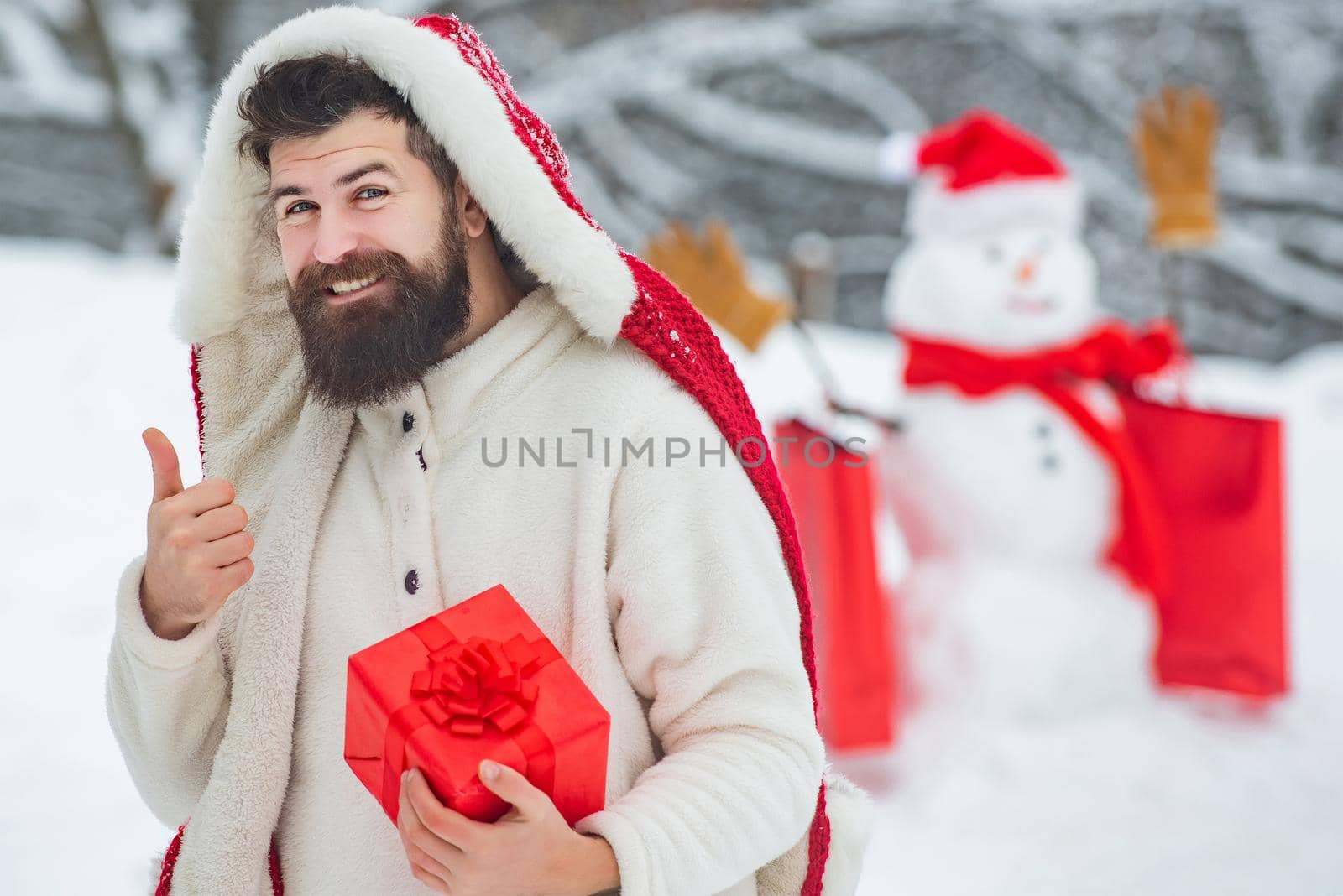 Winter man. Snowman and funny bearded man with gift. Happy father with Christmas gift over winter snowman background. by Tverdokhlib