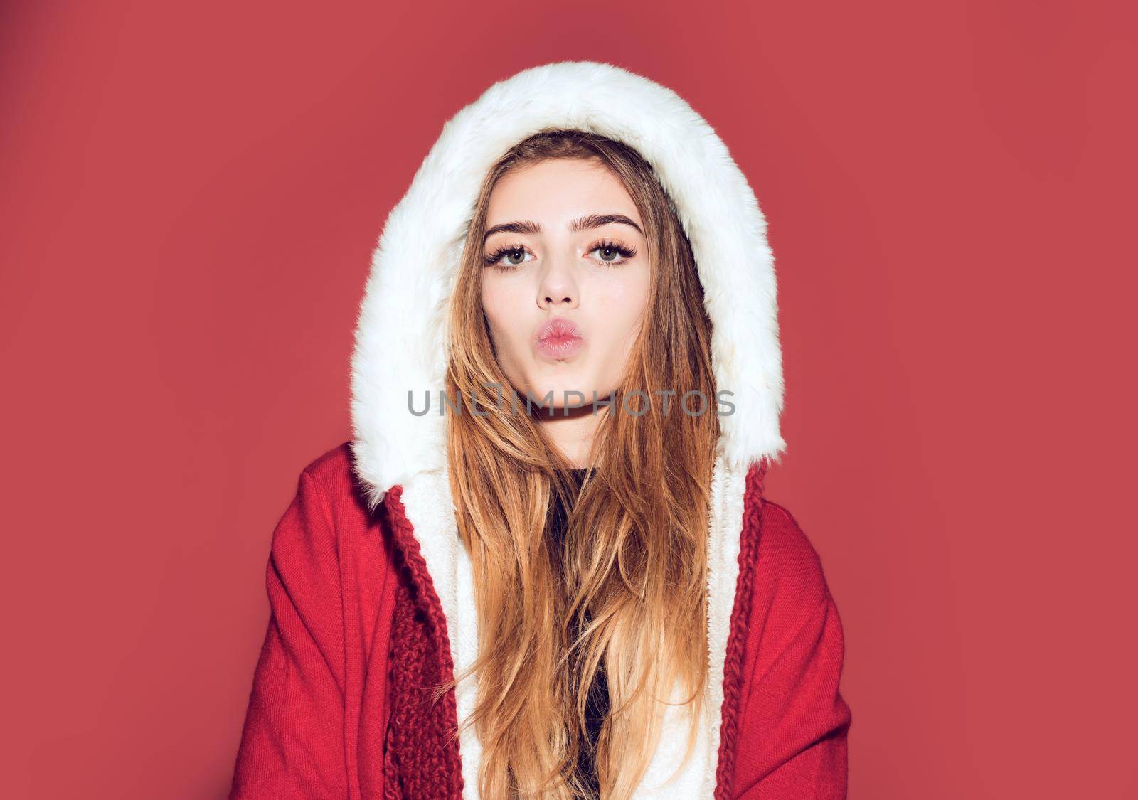 Christmas kiss. Happy girl celebrate new year on red background. Christmas woman in red hat. Woman in santa costume with pretty face.