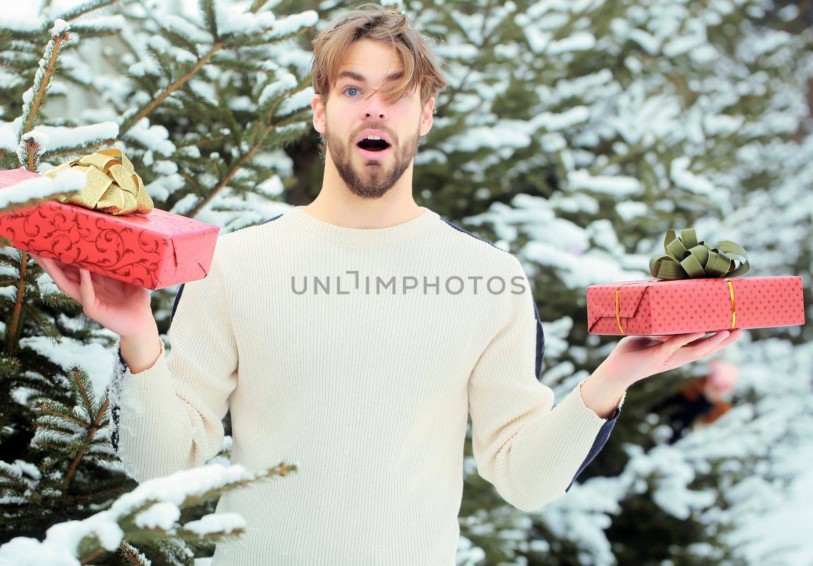 Excited amazed man holding Christmas gift in snow wood outdoor. Merry Christmas and happy new year. Macho with presents on winter day by Tverdokhlib