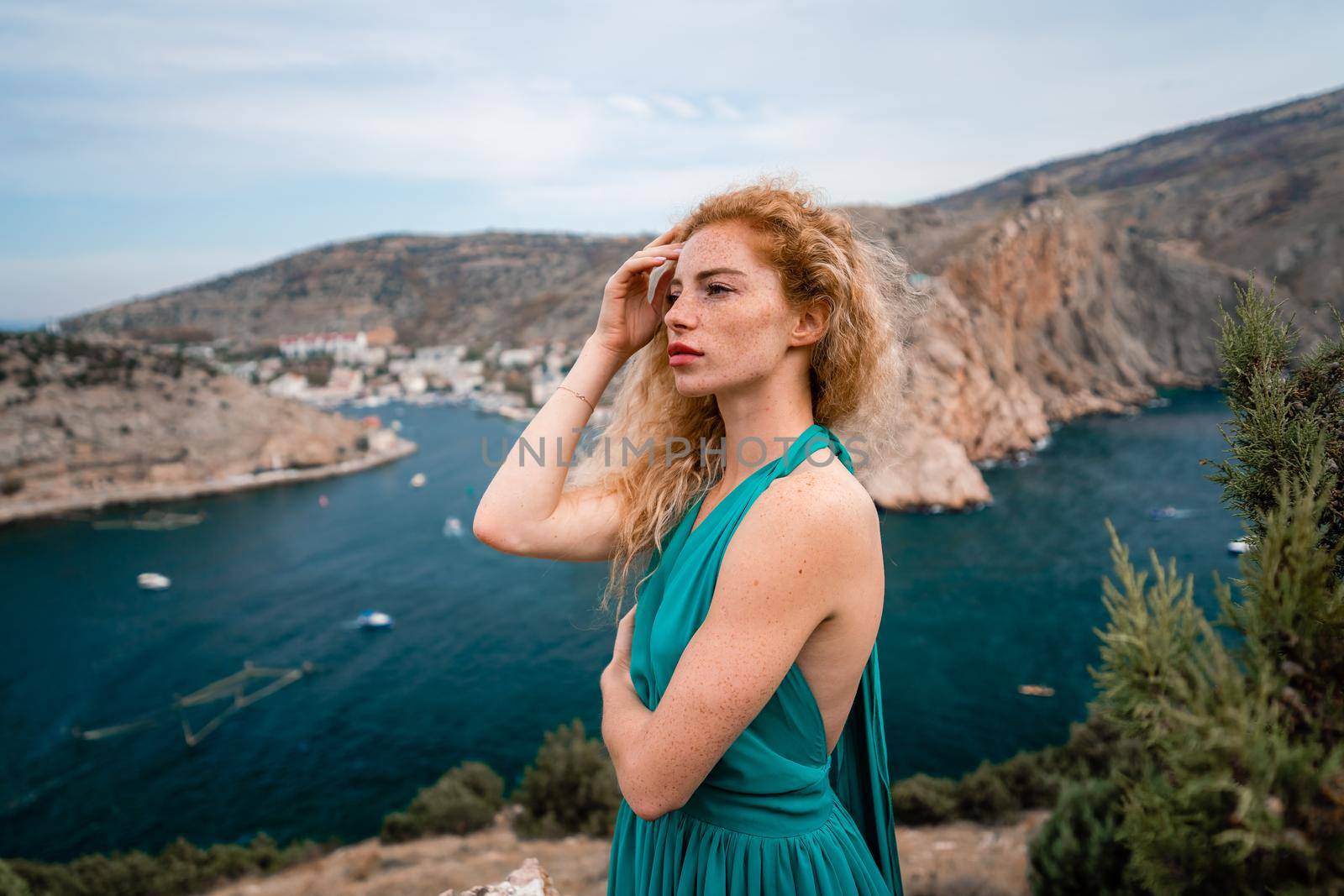 A woman in an emerald dress, a fashion model with long silk wings in a flowing dress, flying fabric on the embankment. by Matiunina