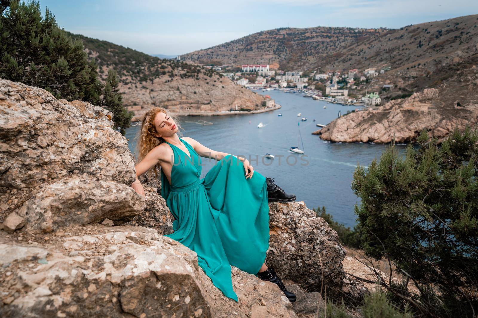 A woman in an emerald dress, a fashion model with long silk wings in a flowing dress, flying fabric on the embankment