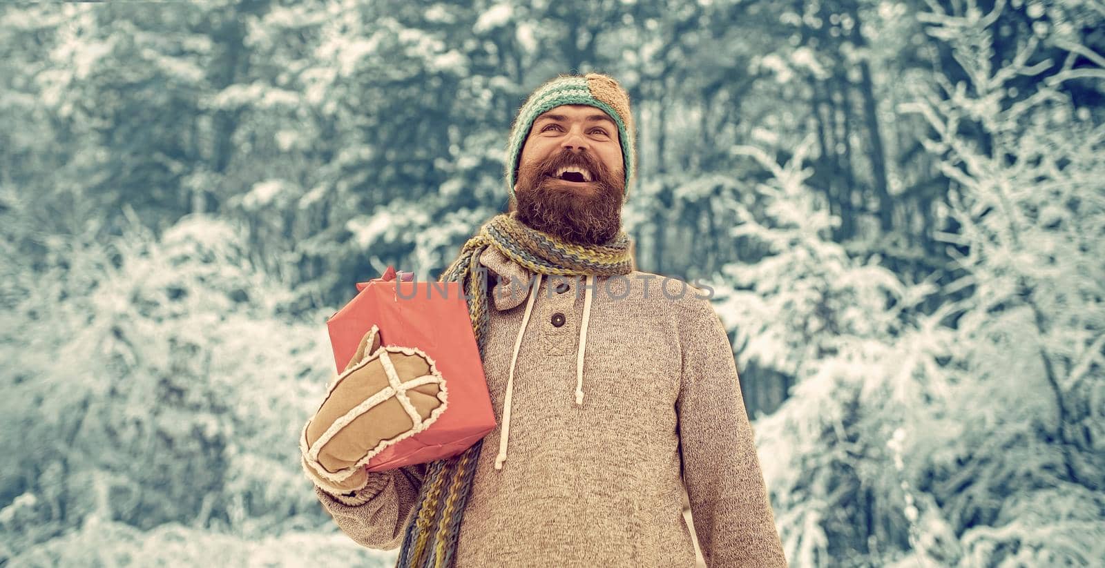 Winter man with beard hold present box. Hipster santa in cold snowy winter forest. Bearded man in santa hat at new year.
