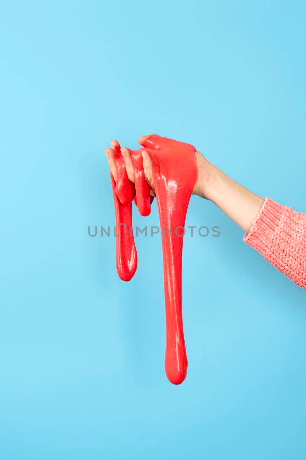 Close up on shiny Red or coral slime in the hand isolated on blue background. Fun and stress relief concept. by esvetleishaya