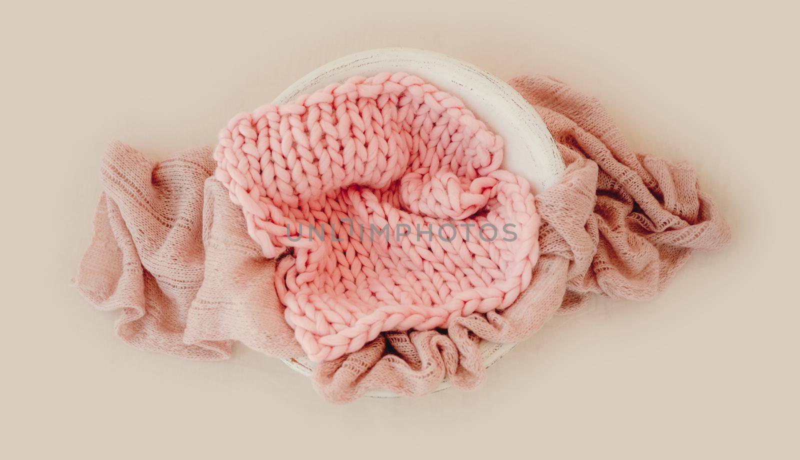 Tiny basin for newborn girl studio photoshoot decorated with pink knitted blanket. Cute decoration for infant child kid photos